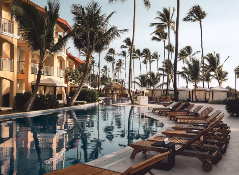 brown wooden lounge chairs near pool surrounded by palm trees